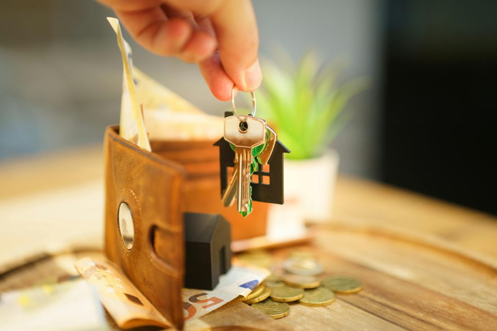 pexels photo 31425035 31425035 Close-up of hand holding a house key with a wallet and coins, symbolizing real estate investment.